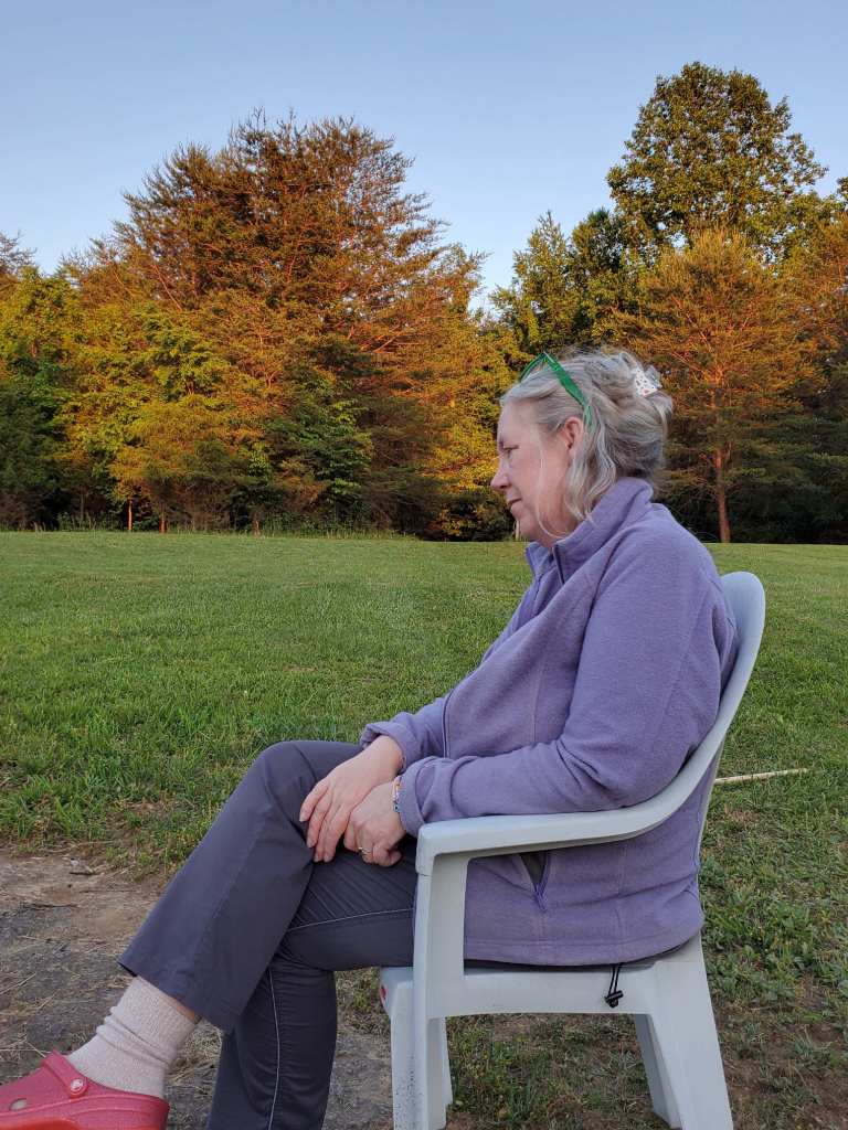 A woman sitting contemplatively with a forest behind her.